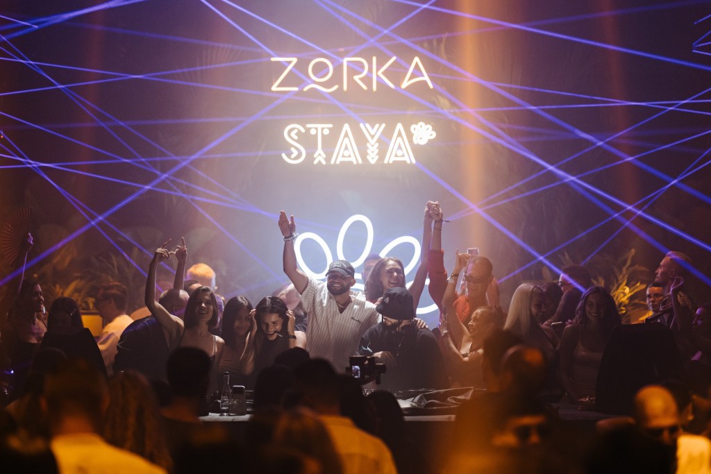 一群人在夜店裡慶祝，背景有彩色激光燈光和'ZORKA STAYA'的標誌。
